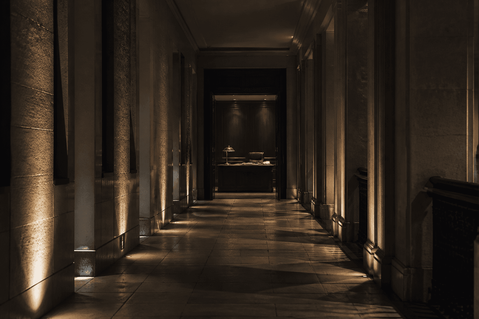 A dark limestone corridor opening onto a quietly lit private desk — the invitation to step into the infrastructure.